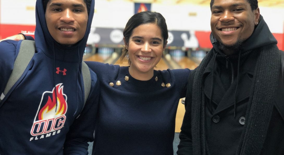 Three people, standing in front of the UIC Bowling Alley, smiling at the camera